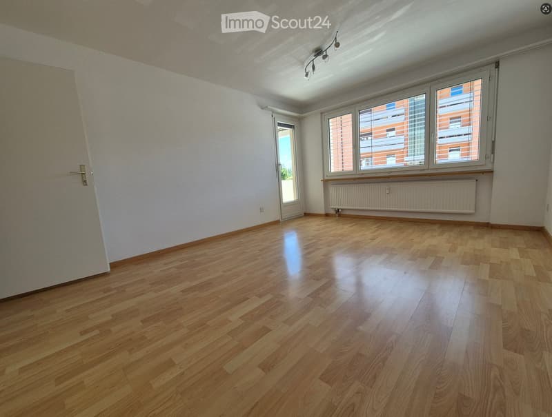 Empty room with wooden flooring, white walls, large windows, and a radiator. No furniture or equipment present.