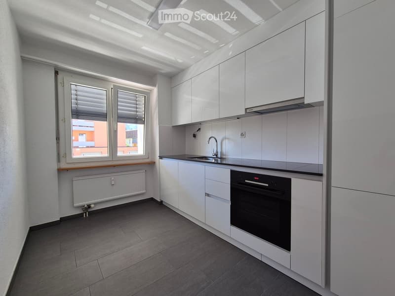 Modern kitchen with white cabinets, a black oven, a sink with a faucet, and a window with blinds.