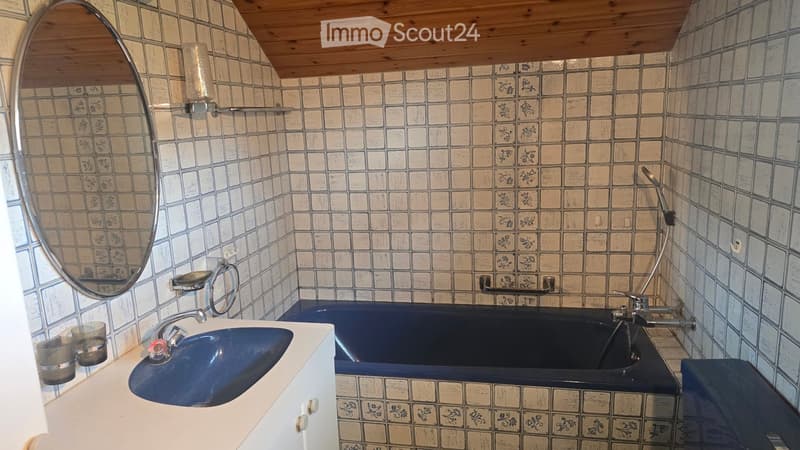 Bathroom with a blue sink and bathtub, tiled walls with floral patterns, a large round mirror, and a wooden ceiling.
