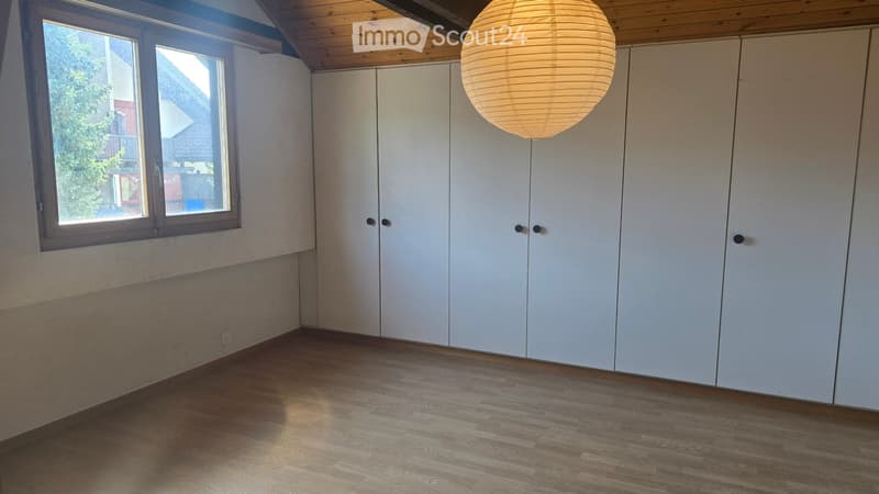 Empty room with wooden flooring, white built-in wardrobes, and a large window letting in natural light. A round paper pendant light hangs from the ceiling.