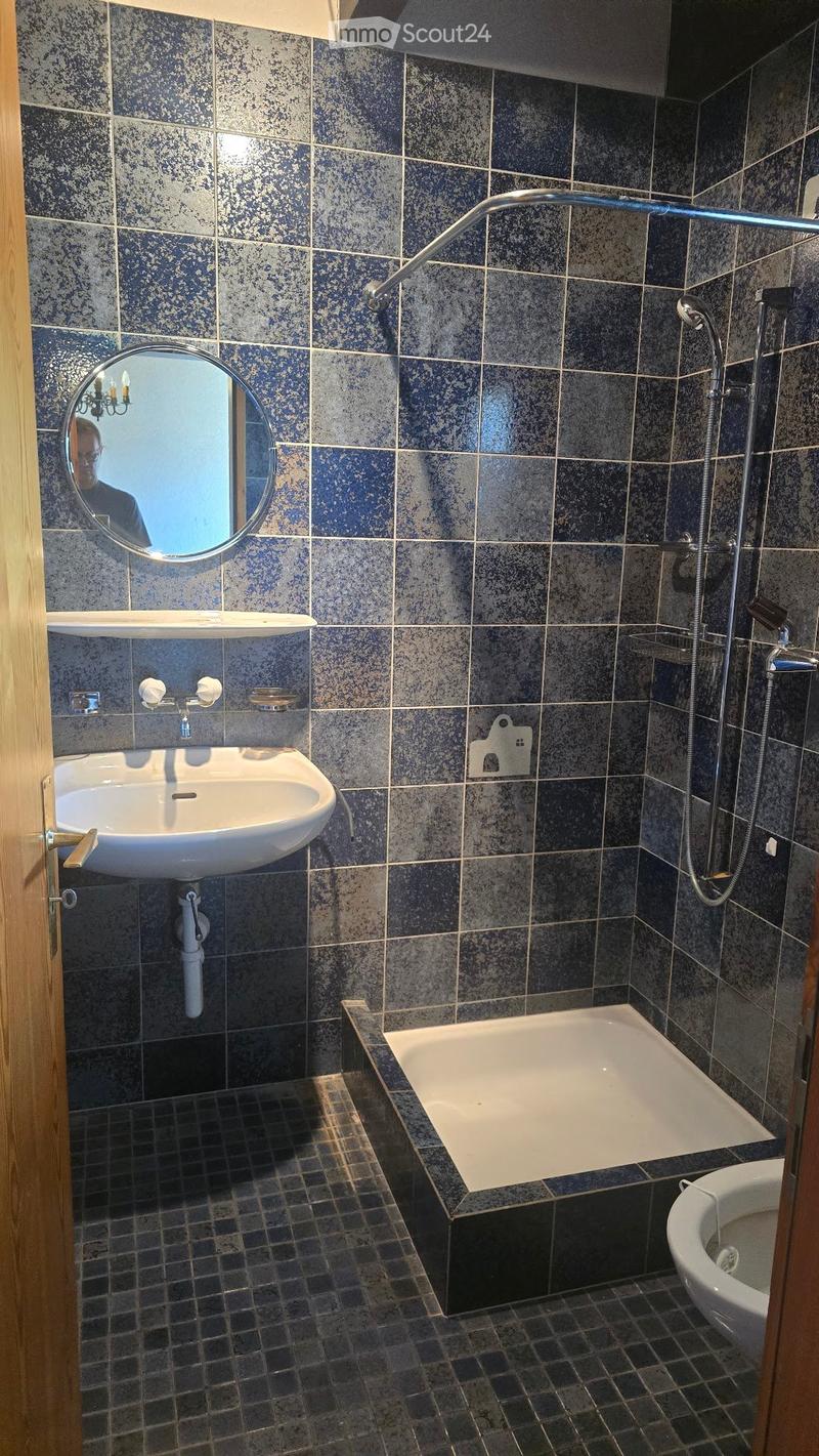 Bathroom with dark blue tiled walls, a white sink, a bathtub, a showerhead, and a round mirror above the sink.