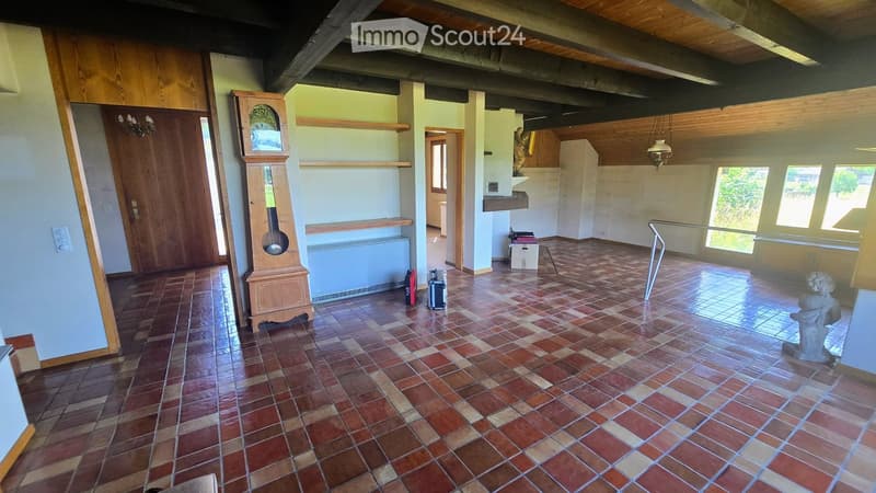 Empty room with exposed wooden beams, tiled floor, and large windows. No furniture or equipment present.