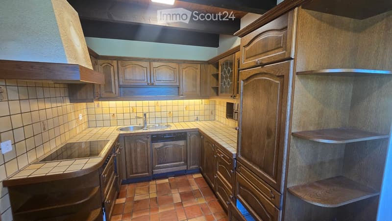 Wooden kitchen with tiled backsplash and countertops, featuring a sink, faucet, and built-in oven.