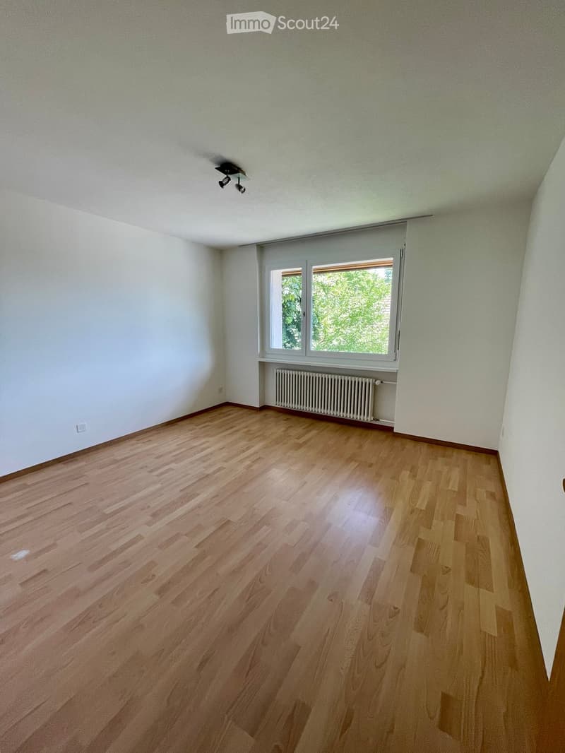 Empty room with wooden flooring, white walls, and a window with a radiator below it.