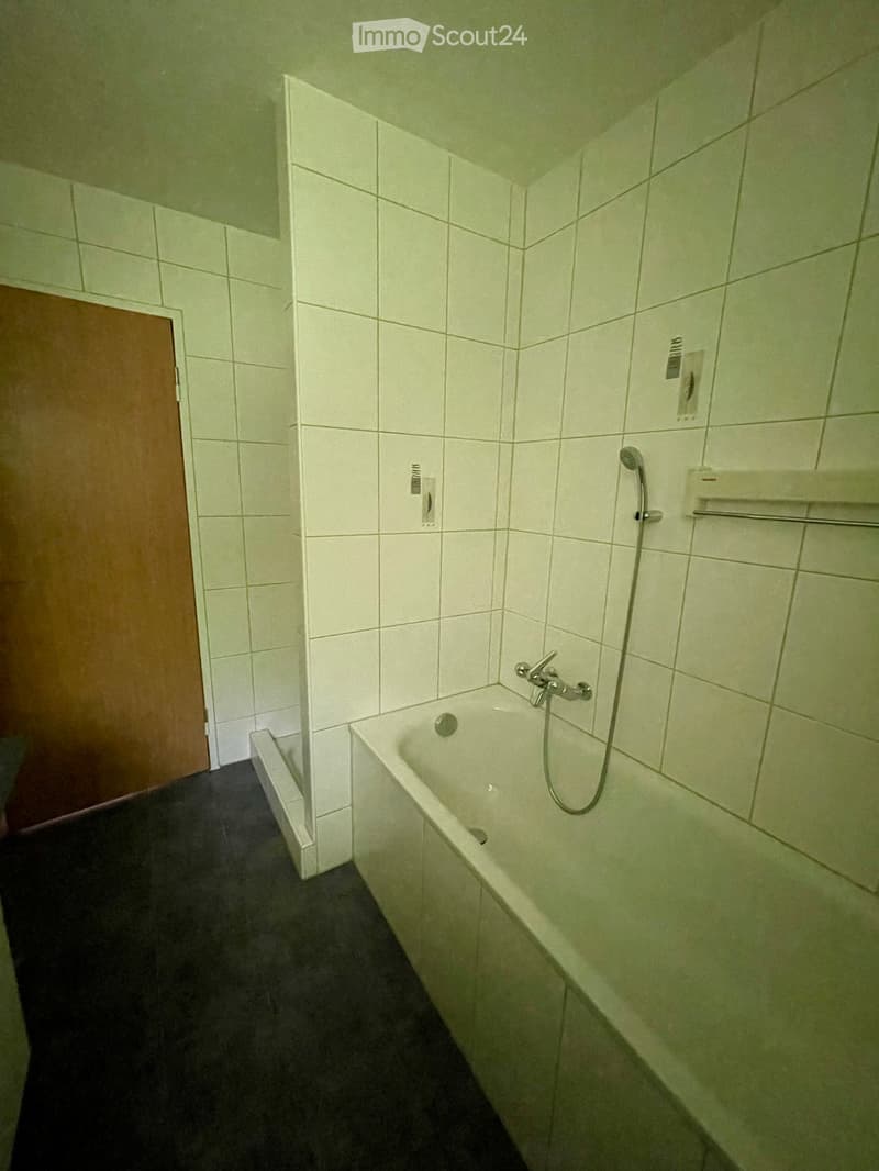 Bathroom with a white tiled wall, bathtub, showerhead, and a wooden door.