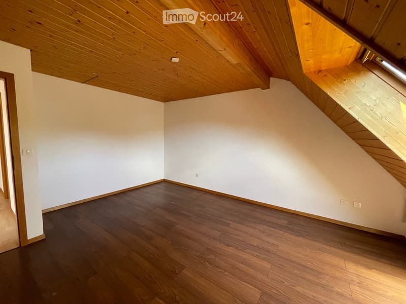 Empty attic room with wooden slanted ceilings, light-colored walls, and dark wooden flooring. No furniture or equipment present.