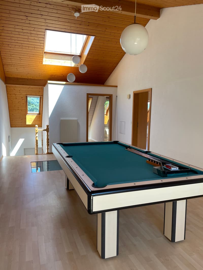 Spacious room with wooden ceiling and floors, large skylight windows, a pool table with green felt surface, and modern pendant lights.