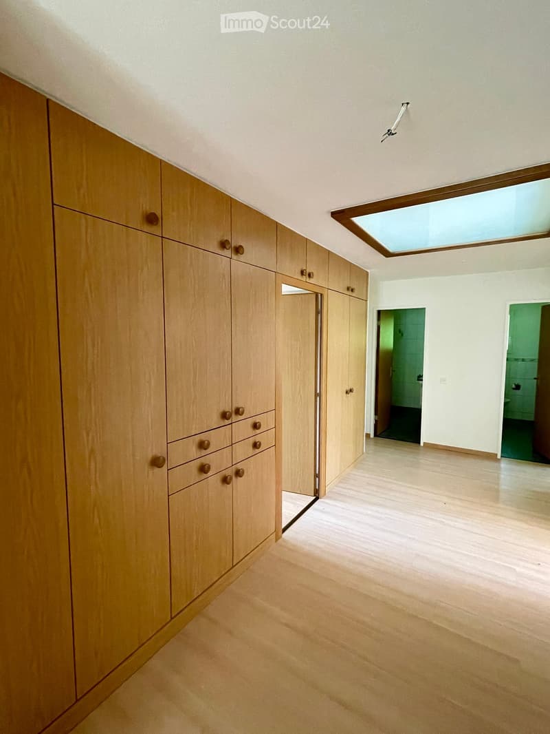 Empty hallway with wooden built-in storage units, light-colored wooden flooring, and a skylight at the far end. Two doors lead to other rooms.
