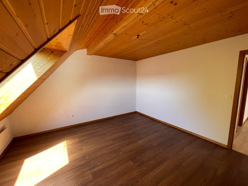 Empty room with wooden flooring and white walls, featuring a slanted wooden ceiling and a skylight window allowing natural light to enter.