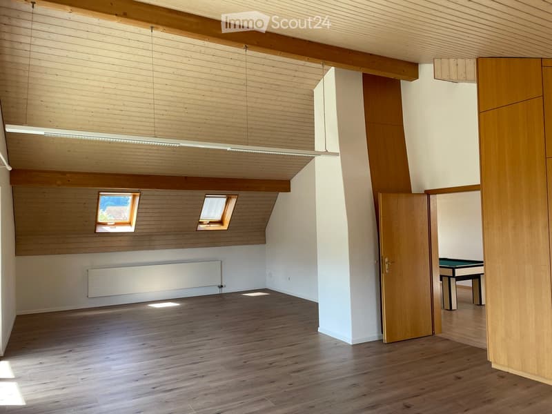 Spacious, unfurnished room with wooden floors, exposed wooden beams, and skylights. A door leads to another room with a pool table.