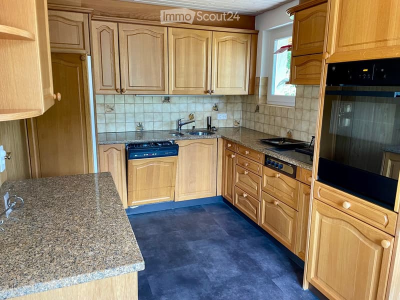 A modern kitchen with light wooden cabinets, granite countertops, a sink, and built-in appliances including an oven and microwave.