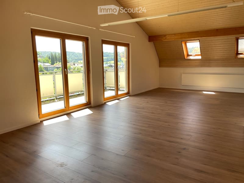 Empty room with wooden flooring, large windows, and sliding doors leading to a balcony.