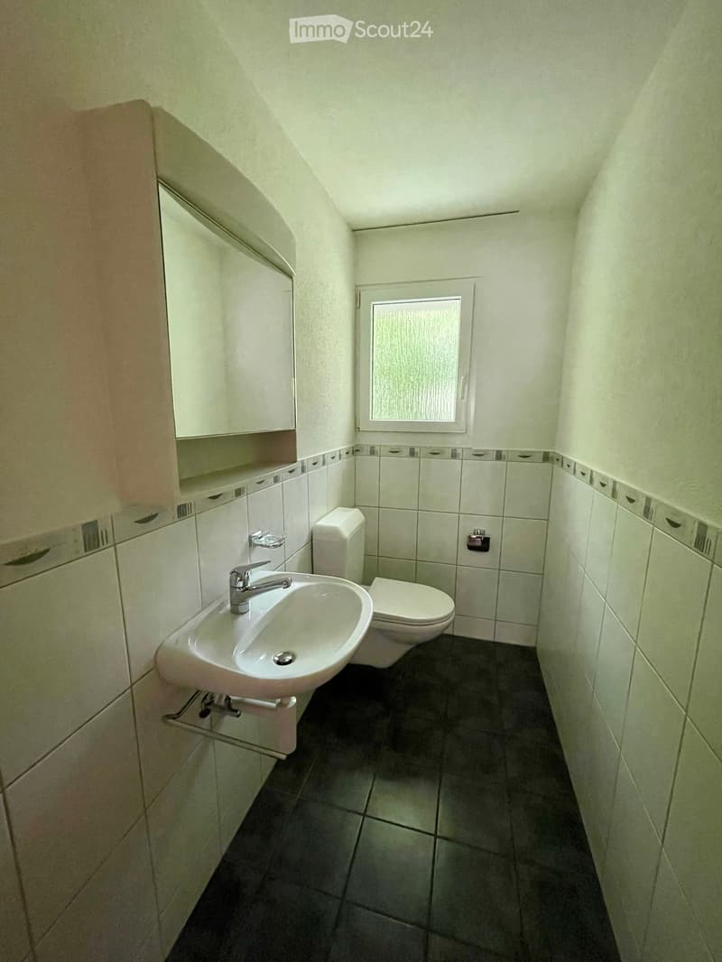 Small bathroom with white tiled walls, dark tiled floor, sink with faucet, toilet, and built-in cabinet.