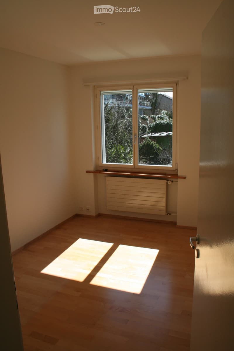 Empty room with wooden flooring, large window with double glass panes, radiator, and a small wooden shelf above it.
