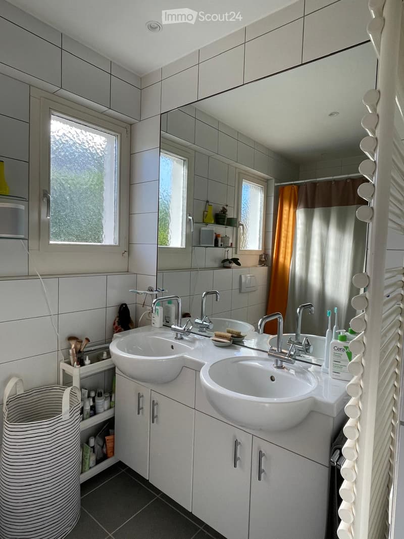 Modern bathroom with double sink, large mirror, white tiles, and various toiletries.