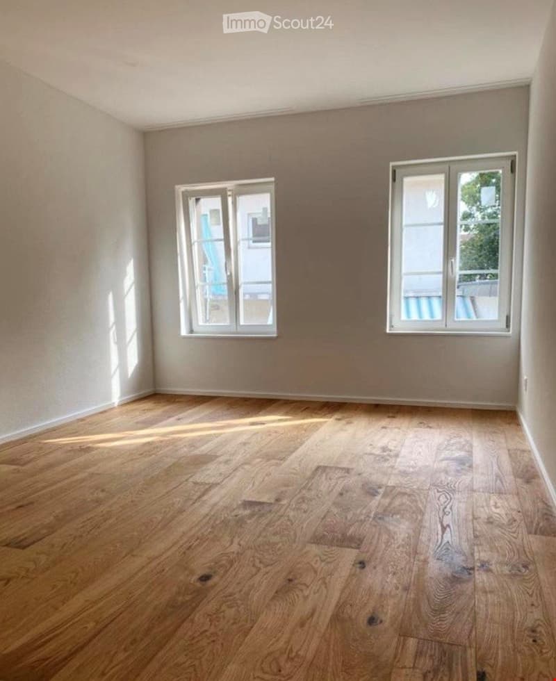 Completely empty room with wooden flooring and two windows, no furniture or equipment.