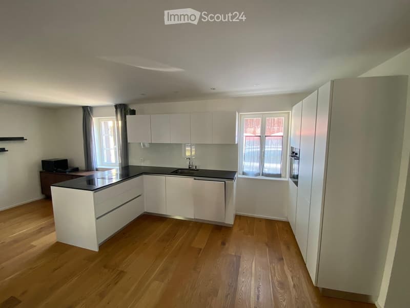 Modern kitchen with white cabinets, black countertop, wooden flooring, and large windows.