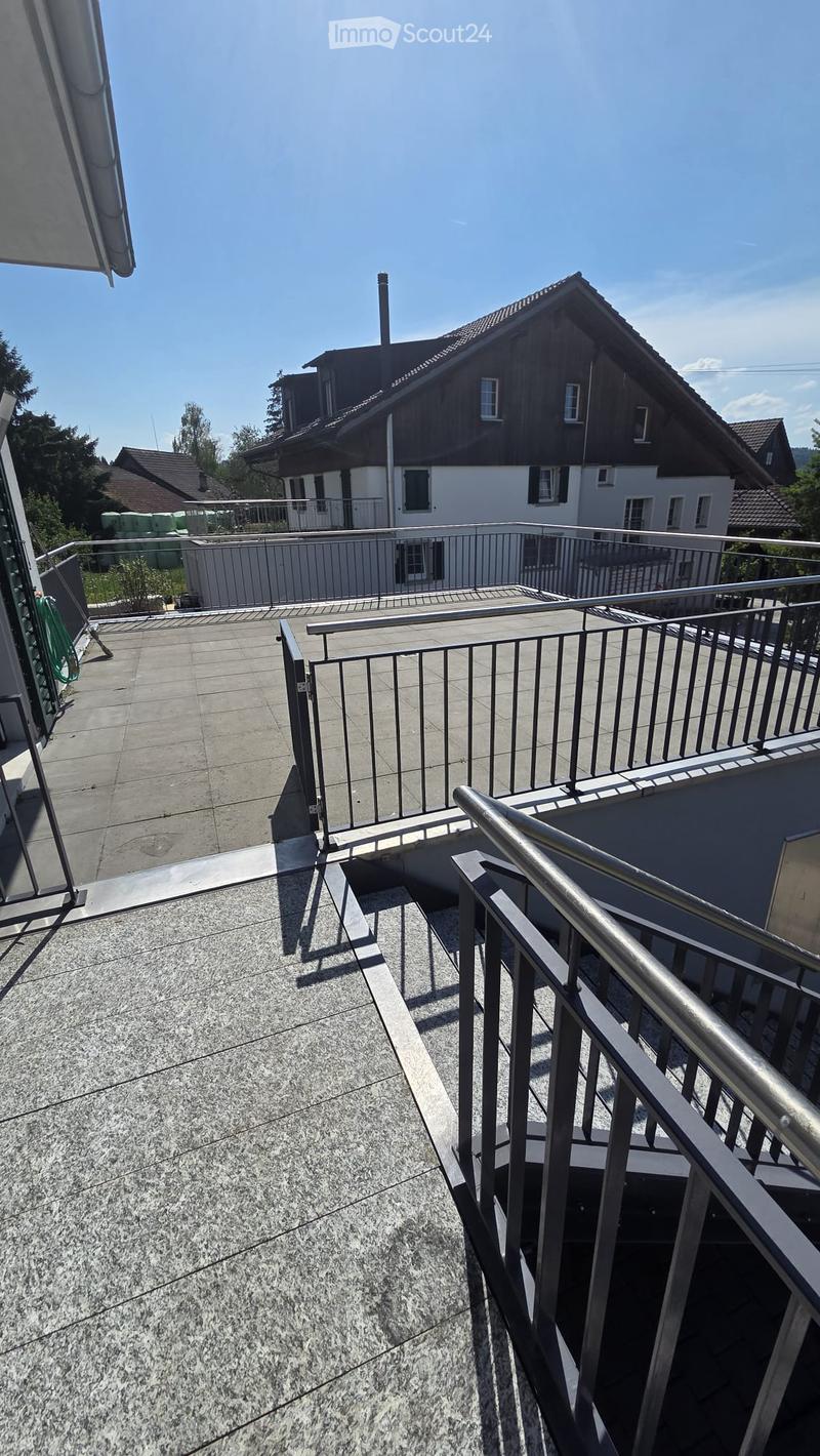 Roof terrace with concrete tiles, metal railing, and steps leading down, overlooking neighboring houses and greenery.