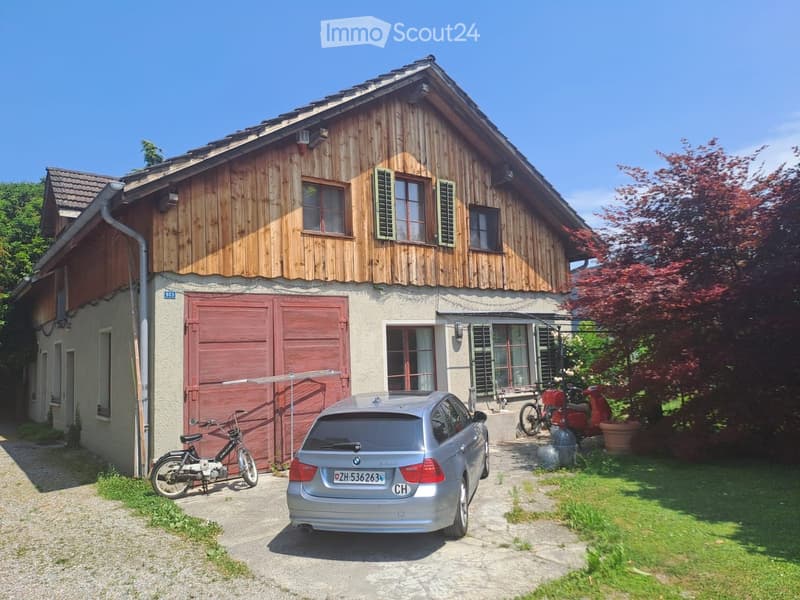 Two-story wooden house with red garage door, multiple windows, and a parked car in front.