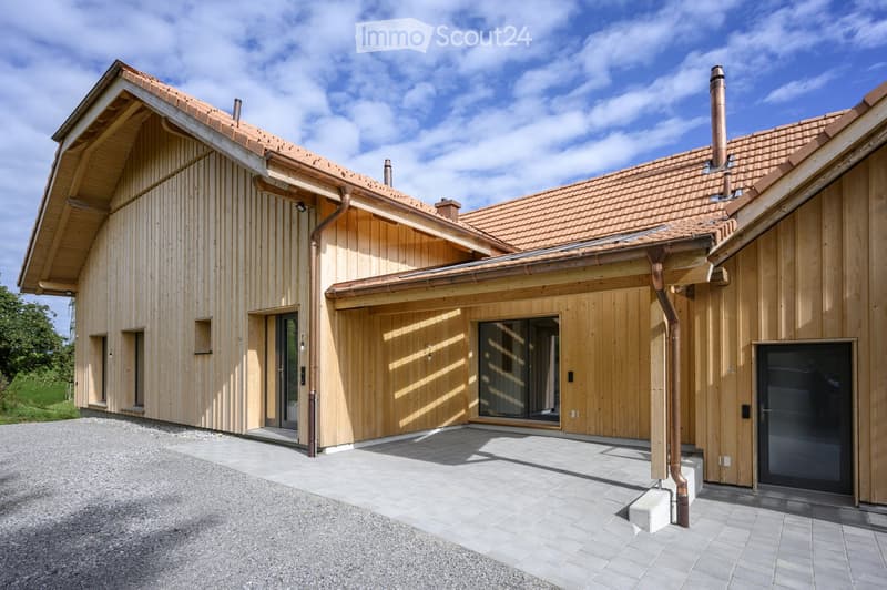 Modern two-story wooden house with a red-tiled roof, large windows, and a covered entrance area.