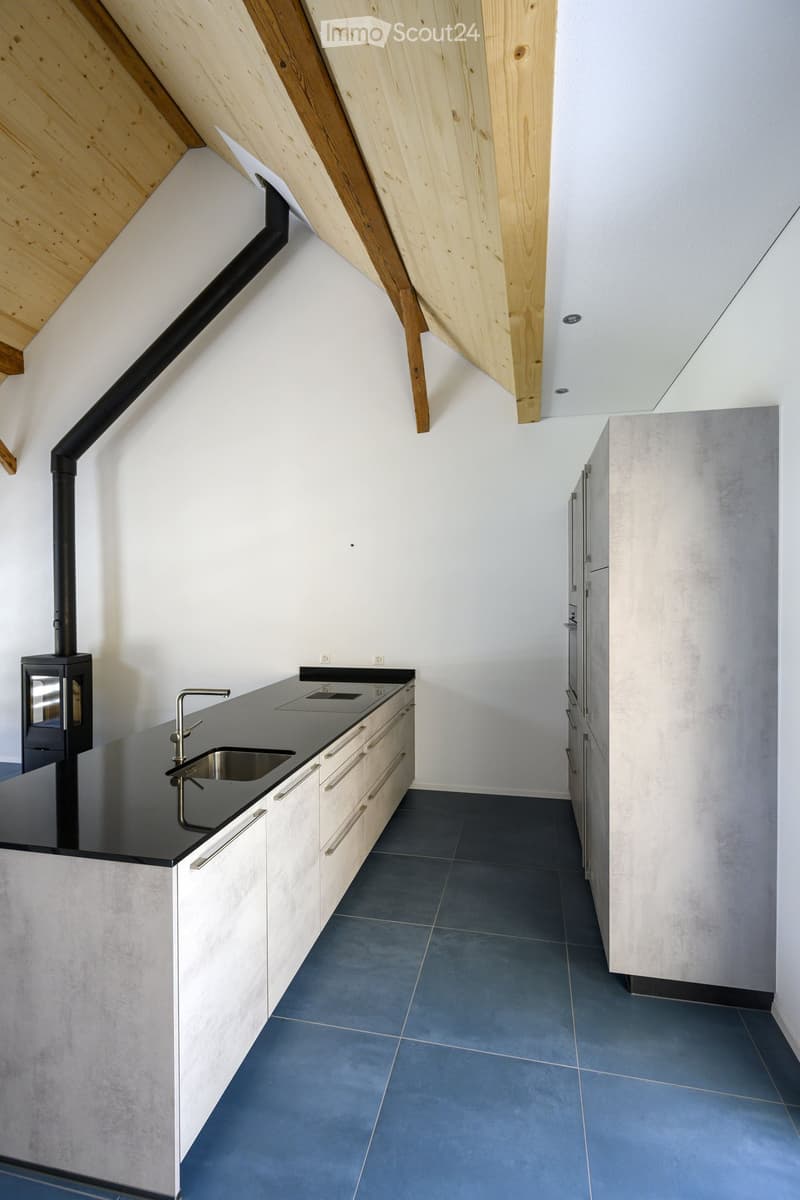 Modern kitchen with sleek black countertops, stainless steel sink, and built-in cabinets. Features a minimalist design with a dark blue tiled floor and white walls.
