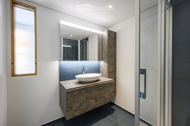 Modern bathroom with a white sink, sleek faucet, large mirror with built-in lighting, and a stylish cabinet with a decorative pattern.