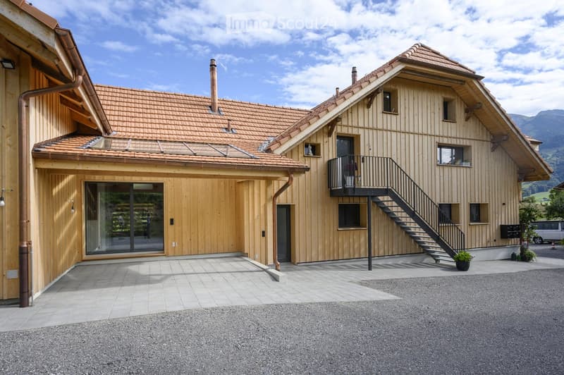 Modern two-story wooden house with a tiled roof, large windows, and a balcony accessible via an outdoor staircase.
