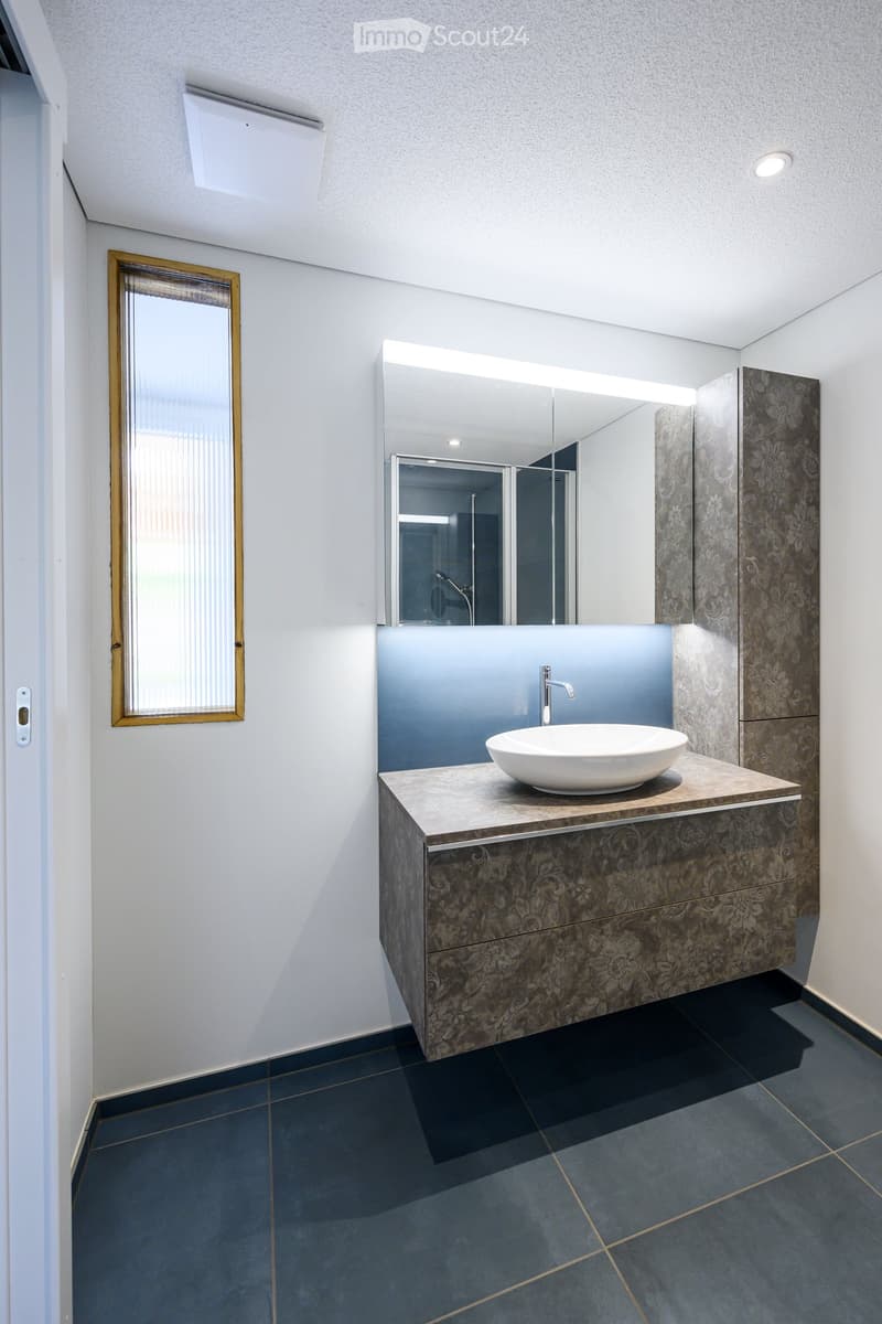 Modern bathroom with a white sink, large mirror, and dark tiled floor.