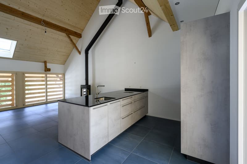 Modern kitchen with a central island, sink, and stove, featuring light wood beams on the ceiling and large windows with wooden shutters.