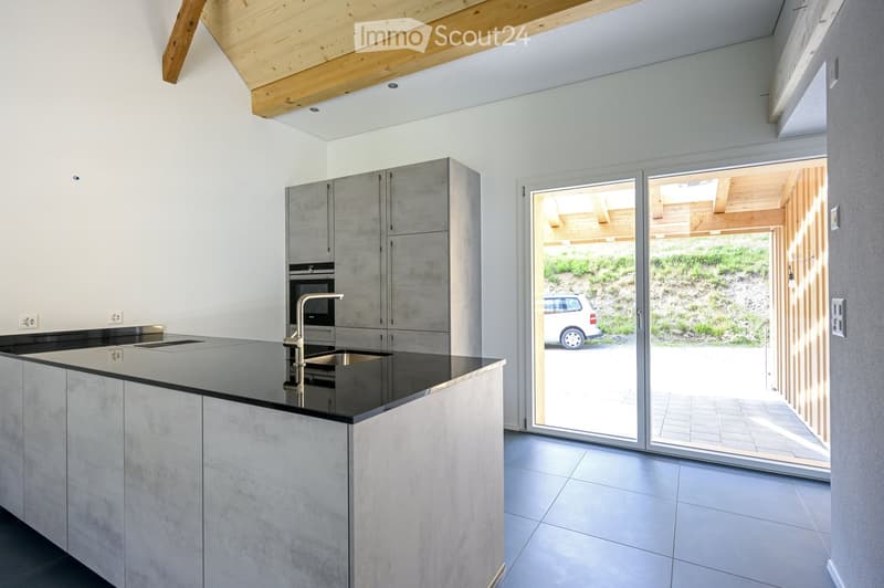 Modern kitchen with sleek, grey cabinets, a black countertop, and a stainless steel sink. Large sliding glass doors open to an outdoor area.