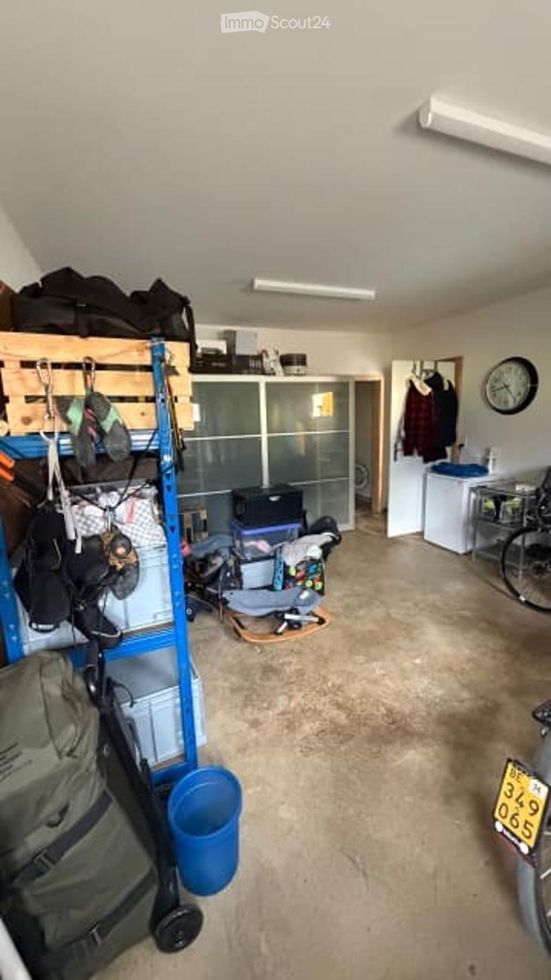 Garage with shelves, storage bins, bicycle, refrigerator, clock, and clothing. The space is organized with various items stored on shelves and the floor.
