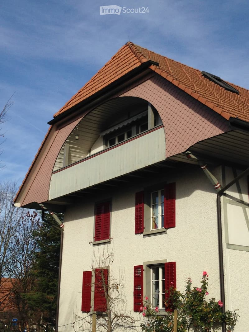 Two-story house with red-tiled roof, white walls, red shutters, and a small balcony on the upper floor.