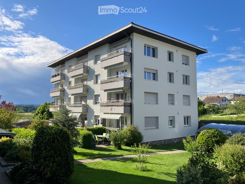 4 story apartment building, white exterior, multiple balconies, garden, trees, and bushes