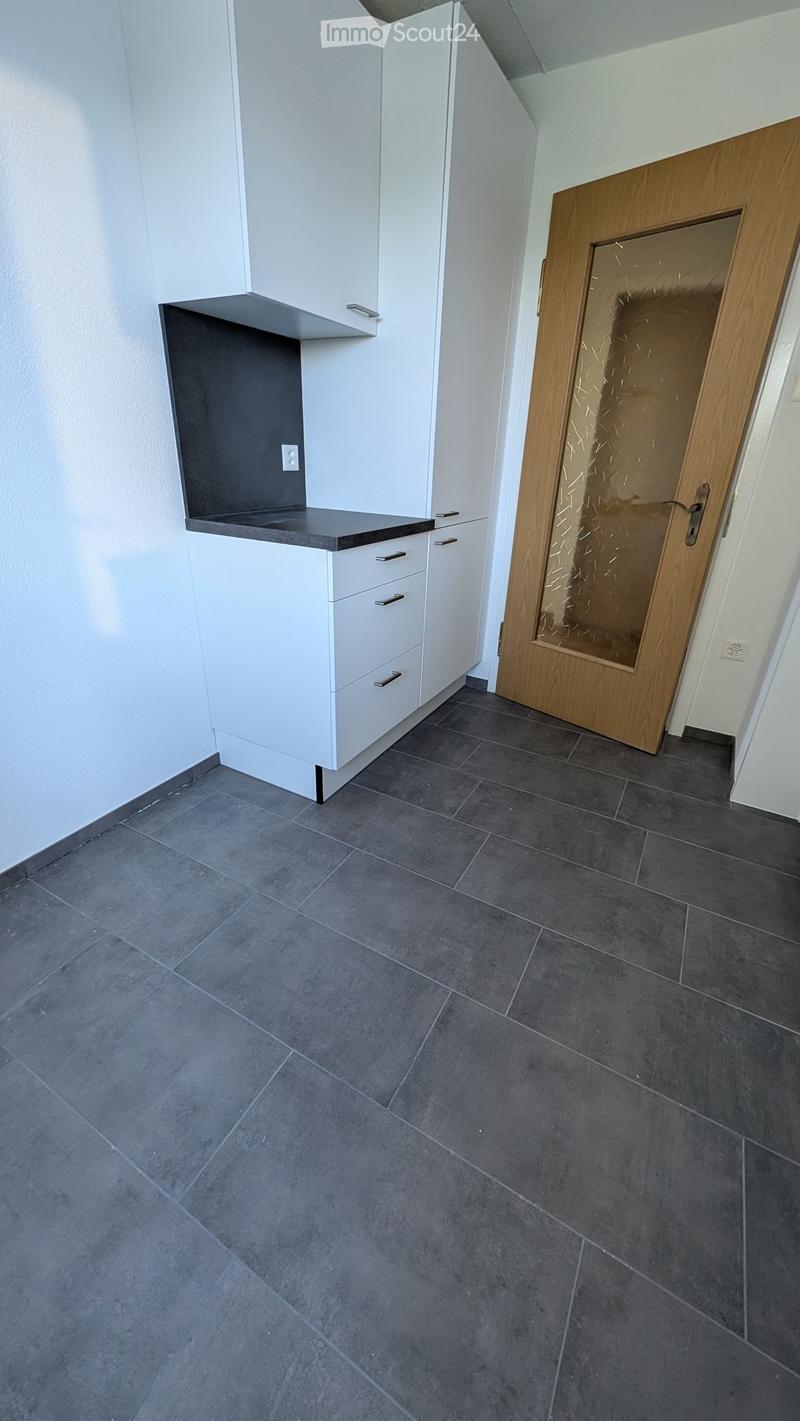 Empty room with dark grey tiled floor, white cabinetry, and a wooden door with a glass panel.