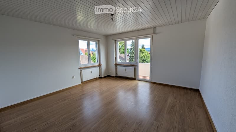 Empty room with wooden flooring, white walls, large windows, and a sliding glass door leading to a balcony.