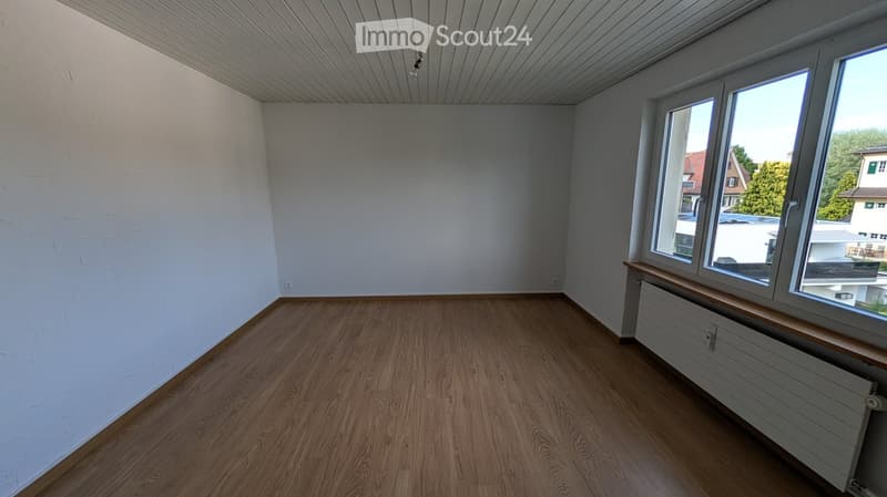 Empty room with wooden flooring, white walls, and large windows offering a view of the outside area.