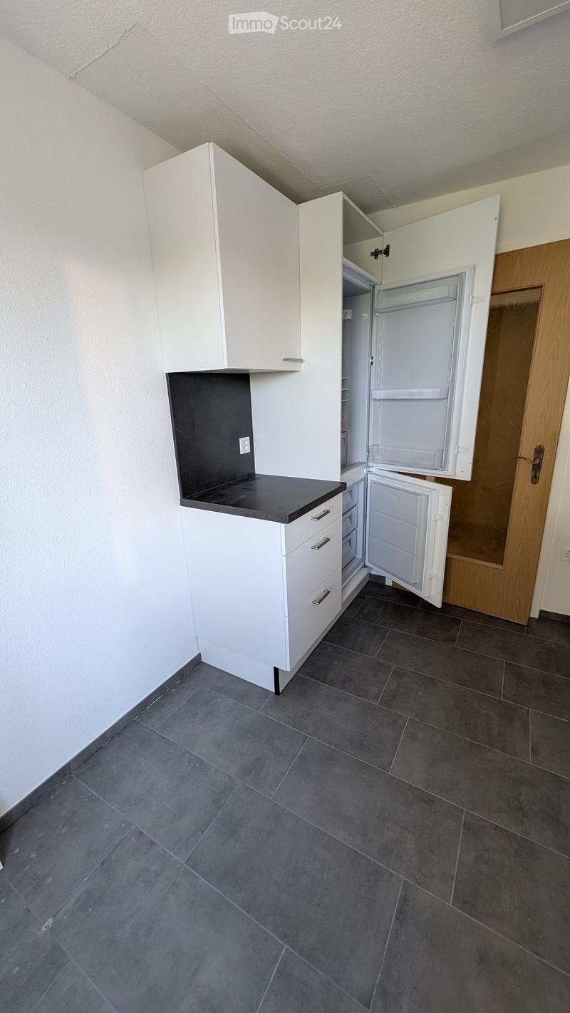 Modern kitchen with white cabinets, black countertop, and an open refrigerator. Dark tiled floor and white walls.