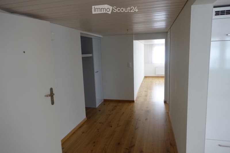 Empty hallway with wooden flooring, white walls, and a closed door on the left side.