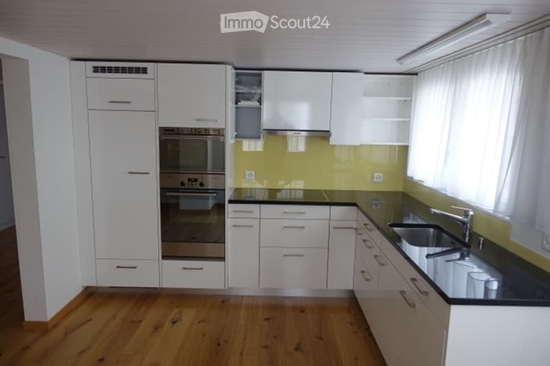 Modern kitchen with white cabinets, stainless steel oven, black countertop, and wooden flooring.