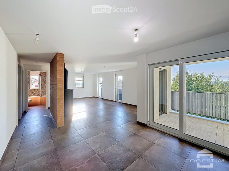 Empty room with tiled floor, white walls, large sliding glass doors leading to a balcony, and a small adjacent bathroom area.
