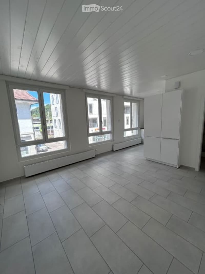 Empty room with tiled floor, white walls, large windows, and a white cabinet.