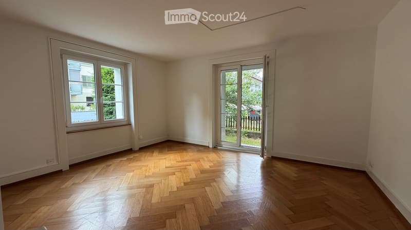 Empty room with wooden herringbone flooring, large window, and sliding glass door leading to a balcony or outdoor area.