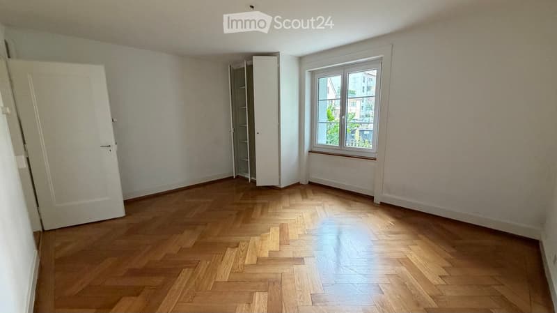 Empty room with wooden flooring, white walls, and a window with a view of the outside. No furniture or equipment is present.