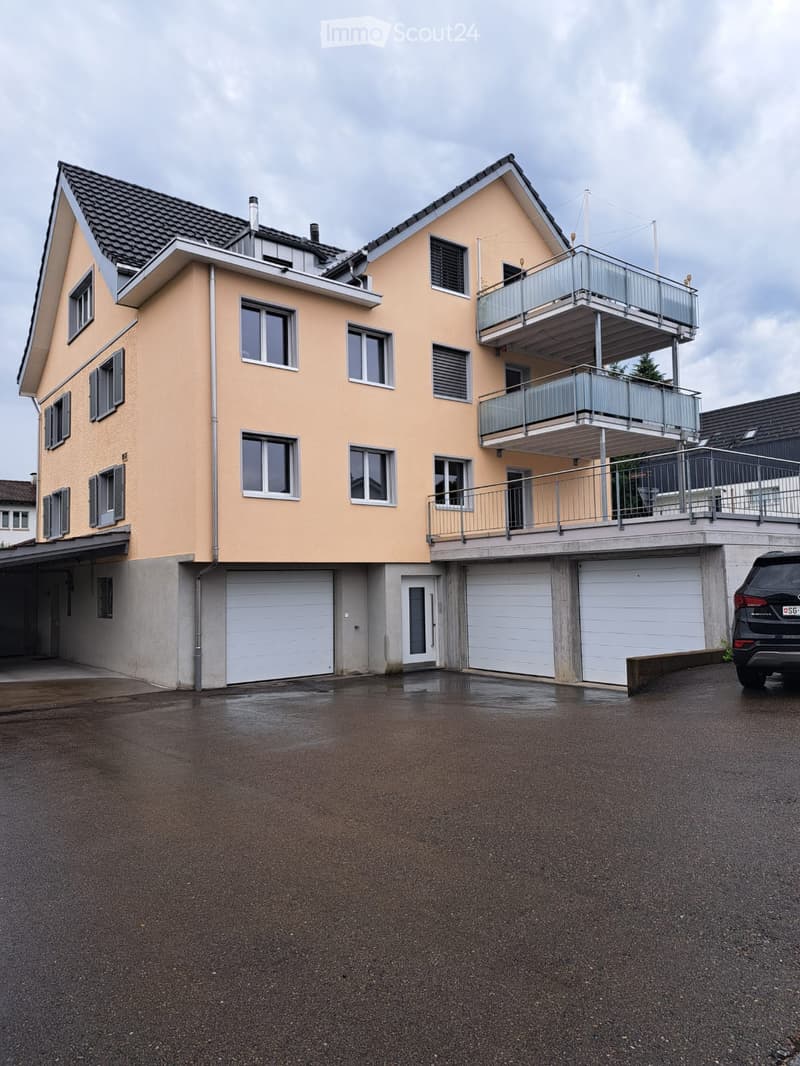 Two-story house with beige exterior, multiple windows, garage, and balcony on the upper level.