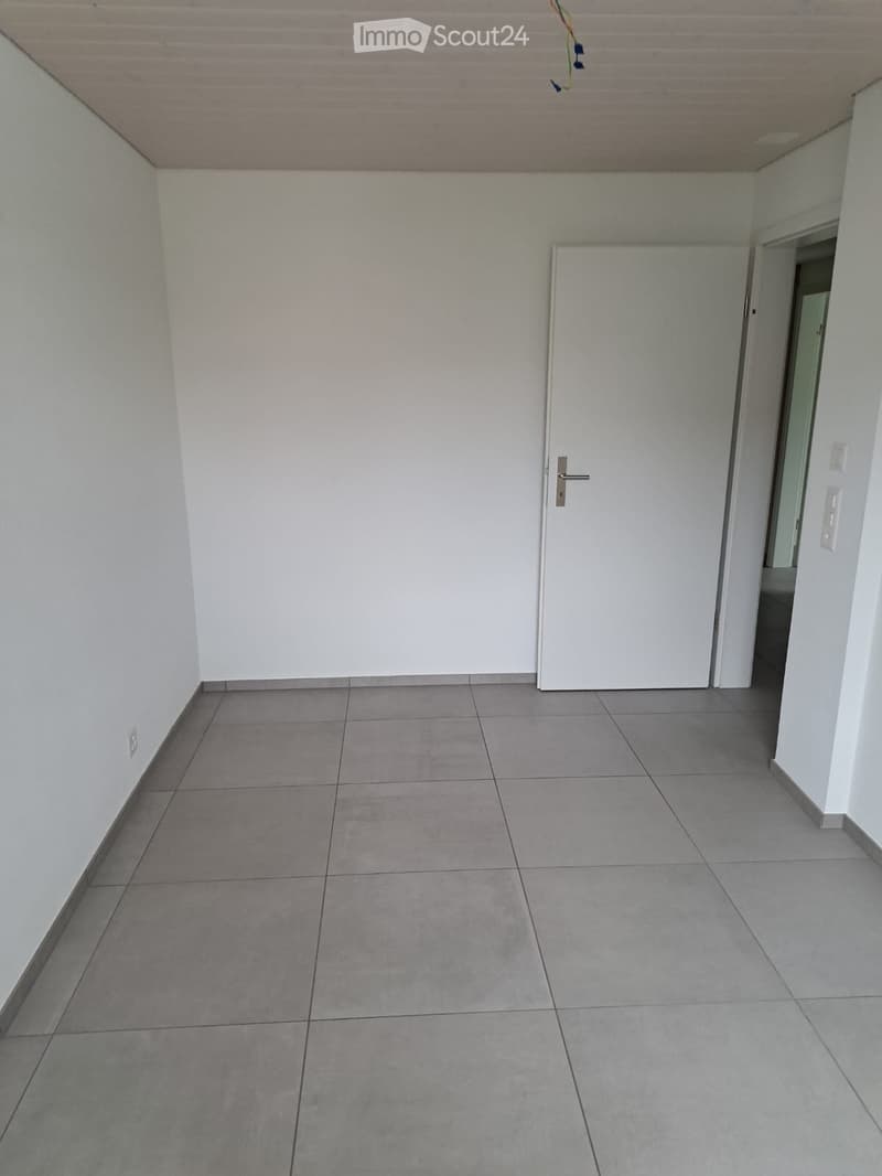Empty hallway with grey tiled floor, white walls, and a white door at the end.