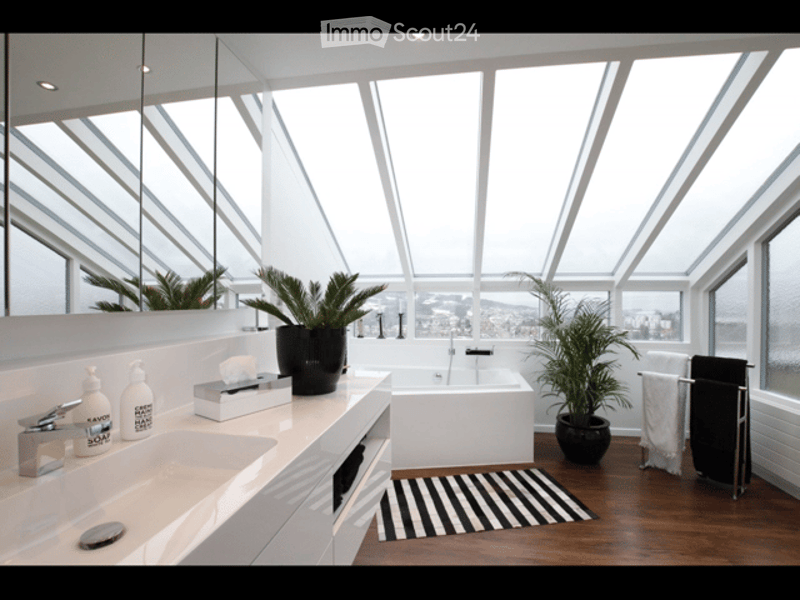 Modern bathroom with large windows offering a view, white sink, bathtub, mirror, towel rack, and decorative plants.