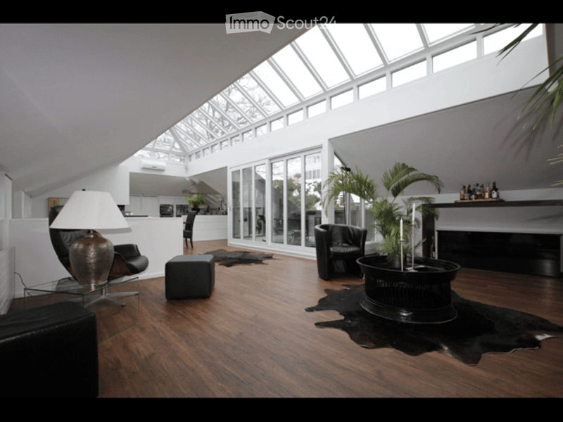 Modern living room with wooden flooring, large skylight, black leather sofa, glass coffee table, floor lamp, fireplace, and potted plants.