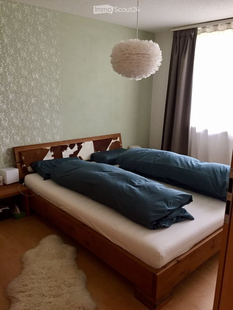 Cozy bedroom with a wooden bed, blue bedding, a nightstand, and a hanging spherical lamp.