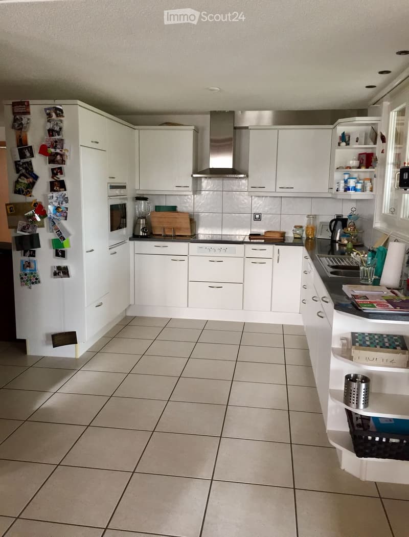 Modern kitchen with white cabinets, stainless steel appliances, and tiled flooring. Features include a central island, a sink, and various kitchen items on the counter.