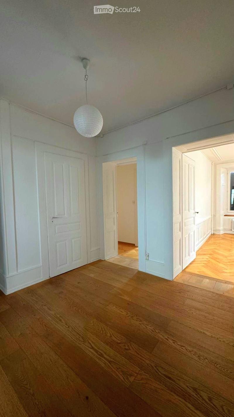 Empty room with wooden flooring, white walls, and a hanging light fixture. Three doors lead to other spaces.